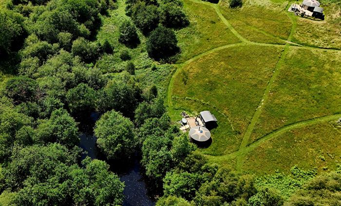 Bird's eye view of 3 yurts in a meadow, surrounded by woodland and with a small lake in top left.